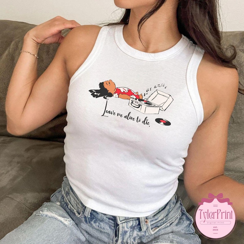 Puede incluir: Camiseta sin mangas blanca con un gr&aacute;fico de una persona acostada junto a un tocadiscos. El texto "Leave me alone to die" est&aacute; impreso en cursiva. La camiseta es sin mangas.
