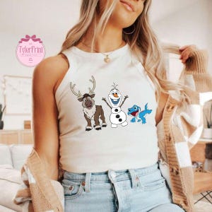 Peut inclure: Un d&eacute;bardeur blanc avec un graphisme color&eacute; de personnages de dessins anim&eacute;s. Le graphisme comprend un renne, un bonhomme de neige et un l&eacute;zard bleu. Le d&eacute;bardeur est sans manches et en mati&egrave;re souple. Le texte "TylerPrint" est visible en haut &agrave; gauche.