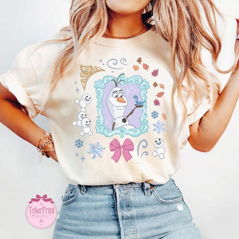 May include: Cream-colored t-shirt featuring a cartoon illustration of Olaf from Frozen, framed in a teal border. The design includes snowflakes, a pink bow, and the text "TylerPrint" in a pink circle.