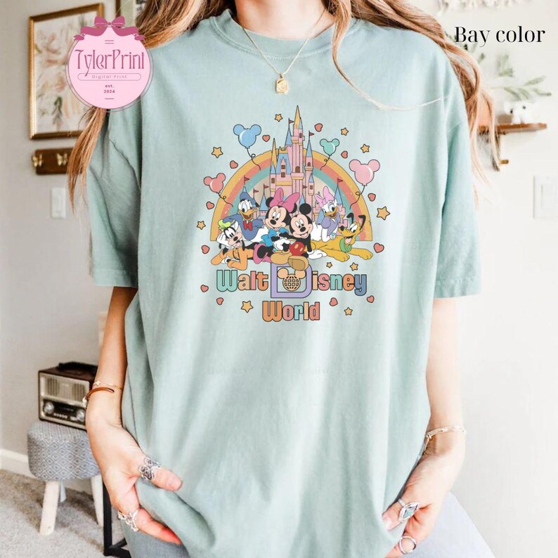 May include: A light blue t-shirt with a retro-style graphic of Mickey Mouse and friends in front of Cinderella's Castle. The graphic includes a rainbow, stars, and the text "Walt Disney World".