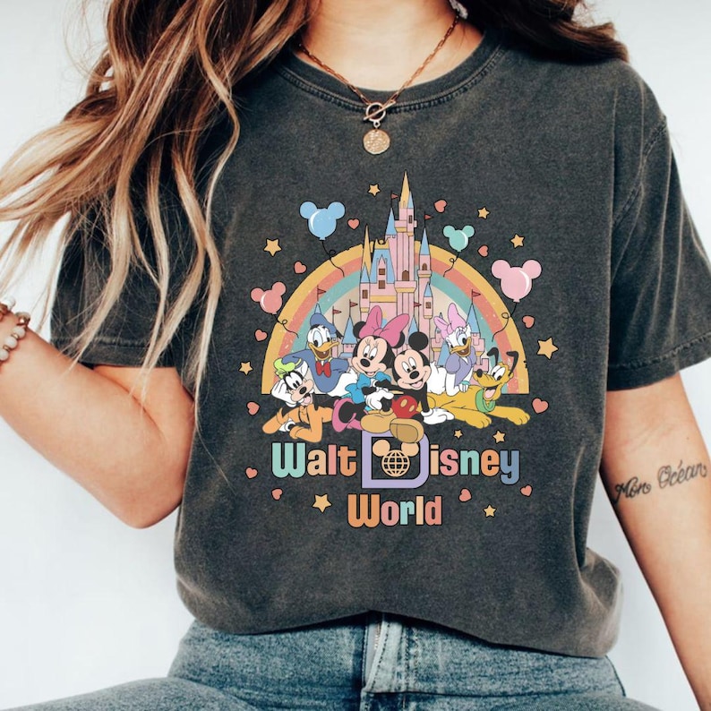 May include: A gray t-shirt with a vintage-style graphic of Mickey Mouse and friends in front of Cinderella's Castle. The graphic includes a rainbow, stars, and hearts. The text "Walt Disney World" is printed below the graphic.
