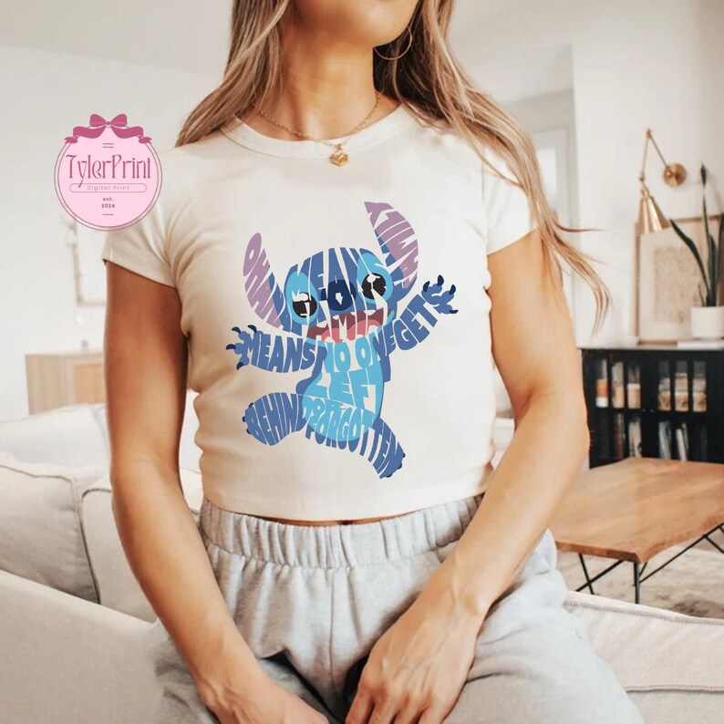May include: White t-shirt with a blue and purple Stitch graphic made of words. The words say "Ohana means no one gets left behind or forgotten".