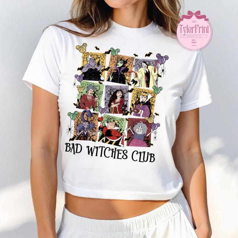 May include: White t-shirt featuring a colorful graphic of various cartoon villains in a grid pattern, with bats and spiders. The text "BAD WITCHES CLUB" is printed in black below the graphic.