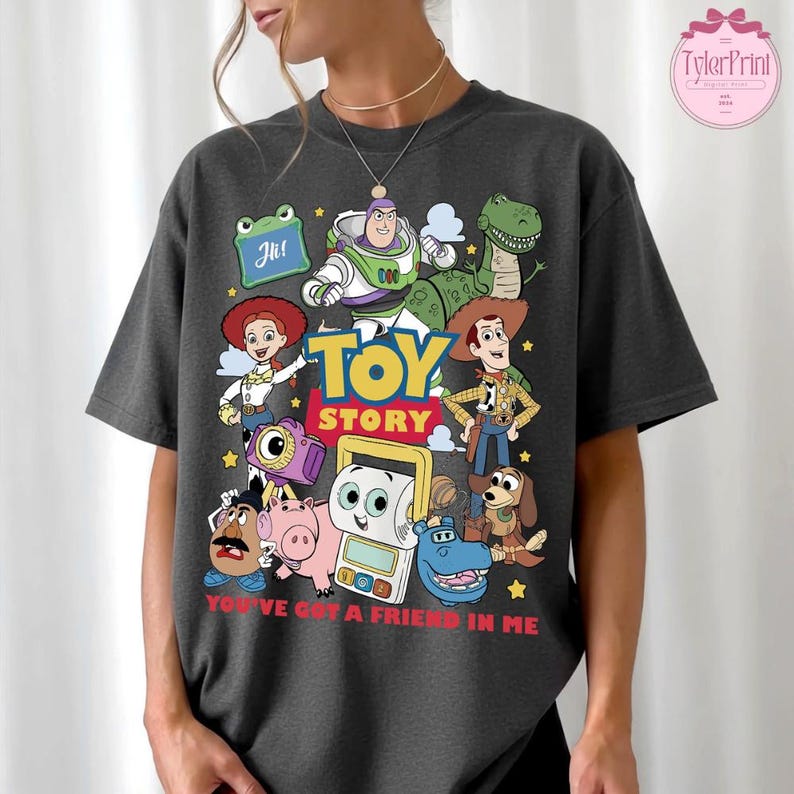 May include: Dark gray t-shirt featuring a colorful graphic of Toy Story characters, including Buzz Lightyear, Woody, and Rex. The words "TOY STORY" are prominently displayed, with the phrase "YOU'VE GOT A FRIEND IN ME" below the characters.