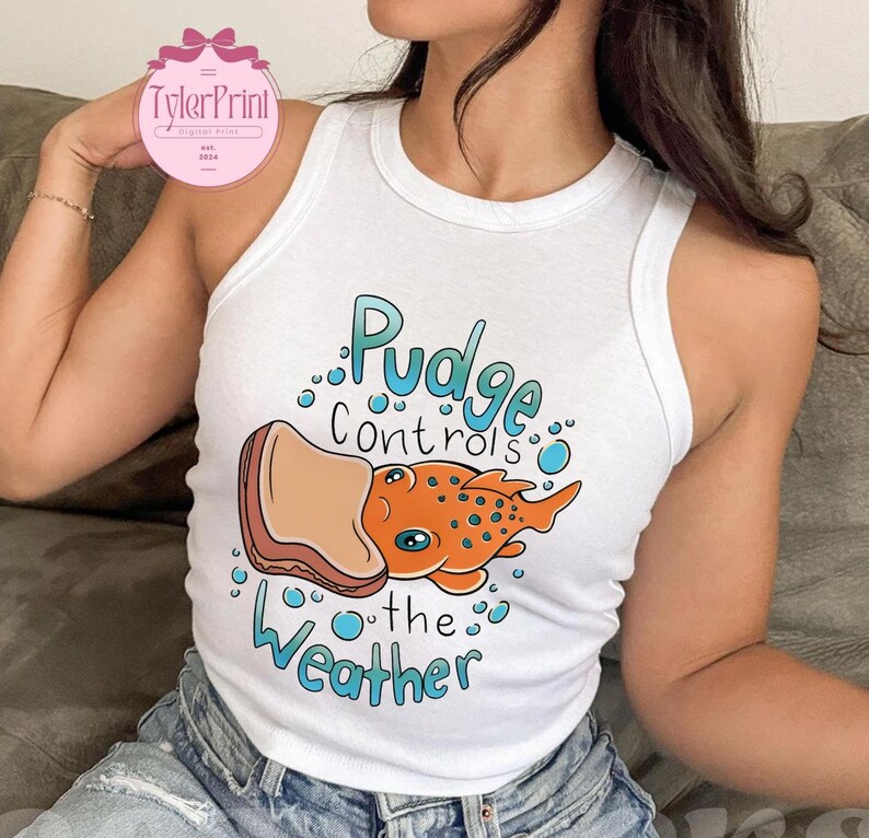 May include: White vest top featuring the text "Pudge Controls the Weather" and a cartoon illustration of an orange fish with blue eyes and a sandwich. The top is sleeveless.