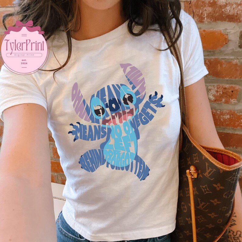 May include: White t-shirt with a blue Stitch character made of words. The words say "Ohana means family and family means nobody gets left behind or forgotten".
