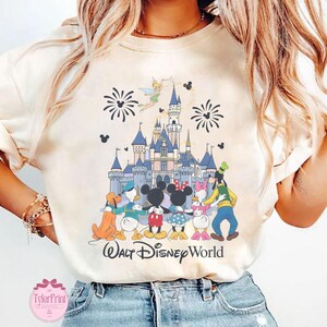 Puede incluir: Camiseta color crema con una colorida ilustraci&oacute;n de personajes de Disney frente a un castillo. El dise&ntilde;o incluye Mickey Mouse, Minnie Mouse, Donald Duck, Daisy Duck, Goofy y Campanilla. Las palabras "Walt Disney World" est&aacute;n impresas debajo.