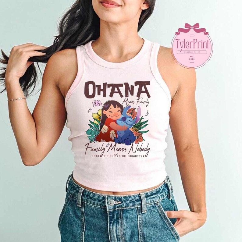 May include: A light pink tank top with the words "OHANA Means Family" and "Family Means Nobody Gets Left Behind or Forgotten". The graphic features a cartoon girl hugging a blue alien-like creature, surrounded by flowers.