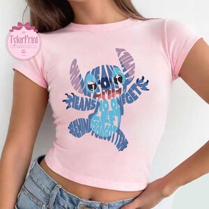 May include: Pink cropped t-shirt with a blue Stitch graphic made of text that says "Ohana means family and family means no one gets left behind or forgotten".
