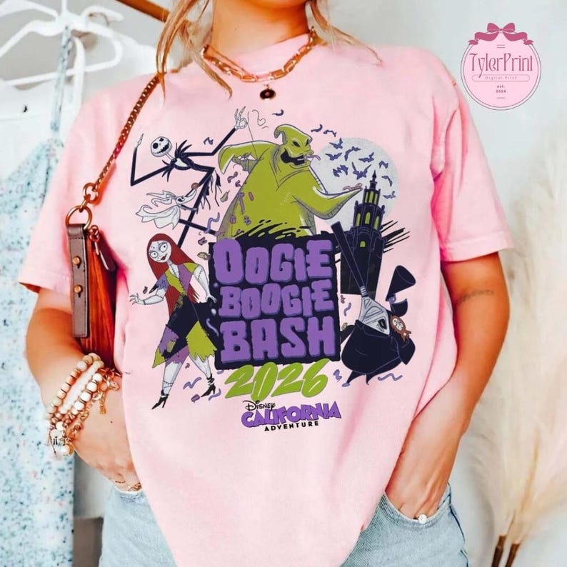 May include: A light pink t-shirt featuring a graphic print of characters from The Nightmare Before Christmas, including Oogie Boogie, Sally, and Jack Skellington. The text reads Oogie Boogie Bash 2026 California Adventure in purple and green.
