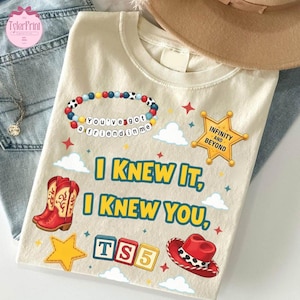 May include: A cream-coloured t-shirt featuring a graphic print with a beaded bracelet reading "You've got a friend in me," a gold sheriff star badge with "INFINITY AND BEYOND," red cowboy boots, a red cowboy hat, and blocks spelling "TS5."
