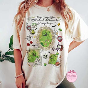 May include: Cream-colored t-shirt featuring a graphic design with the text "Oogie Boogie Bash" and "Well well well, what have we here? Let's oogie boogie!!!". The design includes cartoon characters and Halloween-themed elements.