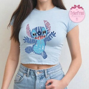 May include: A light blue cropped t-shirt with a blue and purple Stitch graphic. The graphic is made up of words, including "Ohana means family" and "Stitch gets left behind and forgotten".