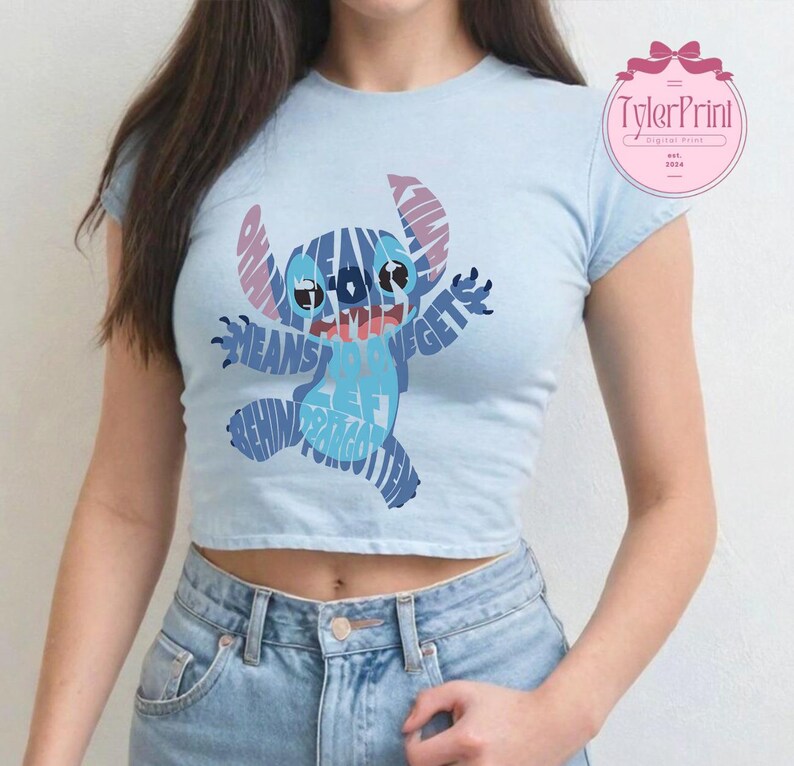May include: A light blue cropped t-shirt with a blue and purple Stitch graphic. The graphic is made up of words, including "Ohana means family" and "Stitch gets left behind and forgotten".