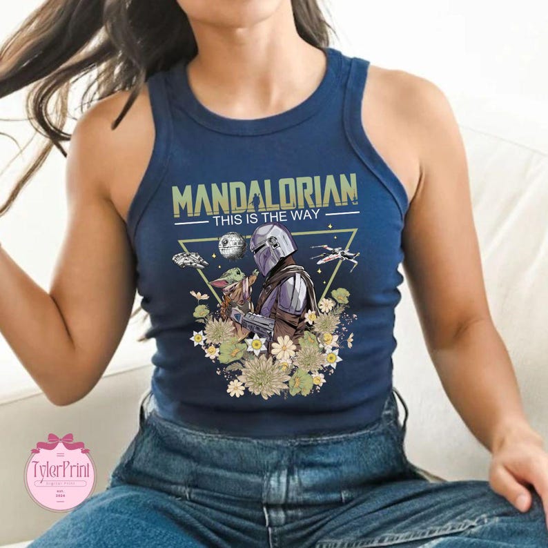 May include: Navy blue tank top featuring a graphic of The Mandalorian and Grogu, with the text "MANDALORIAN THIS IS THE WAY." The design includes a spaceship, the Death Star, and floral elements. The tank top is a sleeveless style.