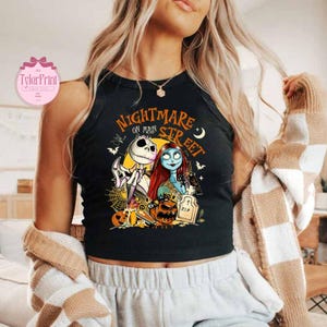 K&ouml;nnte beinhalten: Schwarzes Tanktop mit einer farbenfrohen Grafik aus "Nightmare Before Christmas". Das Design zeigt Jack Skellington, Sally und den Text "Nightmare on Main Street". Ein Top zum Thema Halloween.