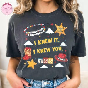 May include: A charcoal grey short-sleeve t-shirt featuring a graphic print with a beaded bracelet reading "You've got a friend in me," a yellow sheriff star badge, red cowboy boots, a red cowboy hat, and the text "I KNEW IT, I KNEW YOU, TS5."