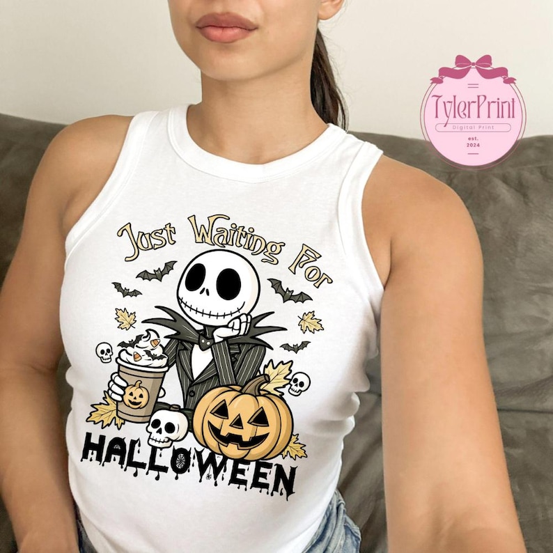 Puede incluir: Camiseta sin mangas blanca con un gr&aacute;fico tem&aacute;tico de Halloween. El dise&ntilde;o incluye un personaje de esqueleto, una calabaza, caf&eacute;, murci&eacute;lagos y el texto "Just Waiting For Halloween."