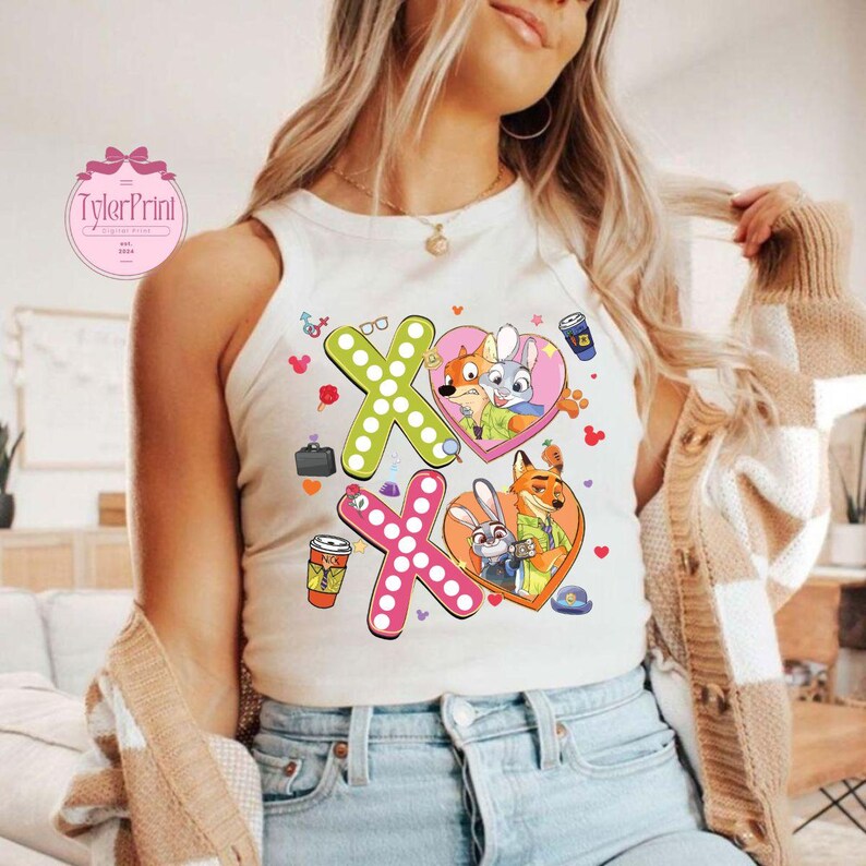 May include: White tank top featuring a colorful graphic design with the text "XO" and cartoon characters. The design includes hearts, coffee cups, and other small illustrations. The tank top is sleeveless.