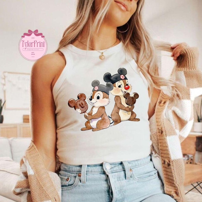 Puede incluir: Una camiseta sin mangas blanca con una ilustraci&oacute;n de dibujos animados de Chip y Chop sosteniendo helados con forma de Mickey Mouse. Los personajes est&aacute;n representados con sus atuendos cl&aacute;sicos. La camiseta sin mangas tiene el logo "TylerPrint" en la parte superior izquierda.