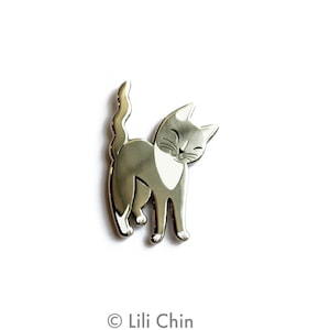 May include: Silver enamel pin featuring a gray and white cat with a smiling face. The cat is standing on its hind legs with its tail curled up.