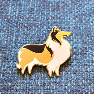 Puede incluir: Un pin de esmalte dorado con un perro Collie de dibujos animados con pelo negro, blanco y marr&oacute;n. El perro est&aacute; de pie sobre sus cuatro patas y mirando hacia la derecha.