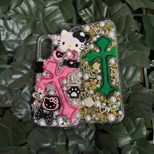 Pode incluir: Duas capas transparentes para telem&oacute;vel com um design de cruz rosa e verde. As capas s&atilde;o decoradas com glitter, p&eacute;rolas e pingentes, incluindo uma personagem Hello Kitty.