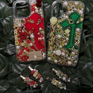 May include: Two clear phone cases decorated with rhinestones, pearls, and charms. One case features a red cross with the word "RED" and the other case features a green cross with the word "GREEN".