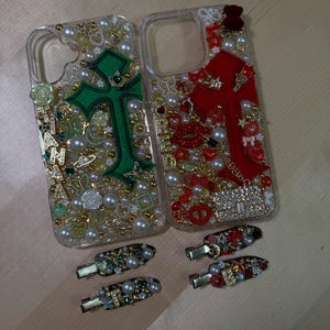 May include: Two clear phone cases decorated with rhinestones, pearls, and charms. One case features a green cross with a crown, the other a red cross. Both cases come with matching hair clips.