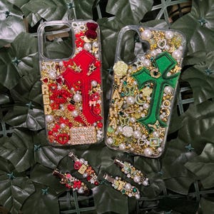 May include: Two clear phone cases with a cross design. One case has a red cross with gold and red embellishments. The other case has a green cross with gold and green embellishments. Both cases have pearls and rhinestones.