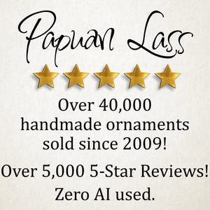 May include: The text Papuan Lass is written in black script above five gold stars. Below this, the text reads: Over 40,000 handmade ornaments sold since 2009! Over 5,000 5-Star Reviews! Zero AI used. The background is a light, textured off-white.