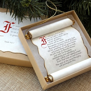 May include: A decorative scroll with text inside a box. The scroll is cream-colored with gold accents and a red initial. The box is tan with a matching lid. The text reads "or unto us a child is born..." and is from Isaiah 9:6-7.