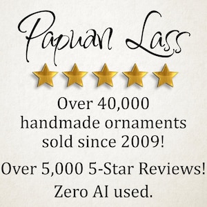 May include: A graphic display featuring the text Papuan Lass in a black script font, followed by five gold stars. Below, black text reads: Over 40,000 handmade ornaments sold since 2009! Over 5,000 5-Star Reviews! Zero AI used.