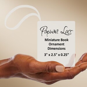 May include: A rectangular white ornament featuring the text Papuan Lass Miniature Book Ornament Dimensions 3 inches by 2.5 inches by 0.25 inches with a white loop at the top for hanging purposes, presented on a neutral background.