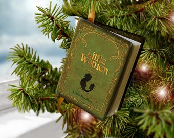 May include: A miniature book ornament titled Little Women by Louisa May Alcott, featuring a green cover with gold filigree borders, a central silhouette illustration of a person reading, and a gold ribbon for hanging on a tree branch.