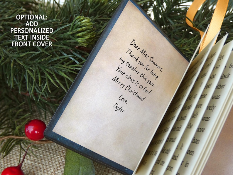 May include: A small, open book with a dark cover and cream-colored pages. The front page features printed text that reads: Dear Miss Summers, Thank you for being my teacher this year. Your class is so fun! Merry Christmas! Love, Taylor.