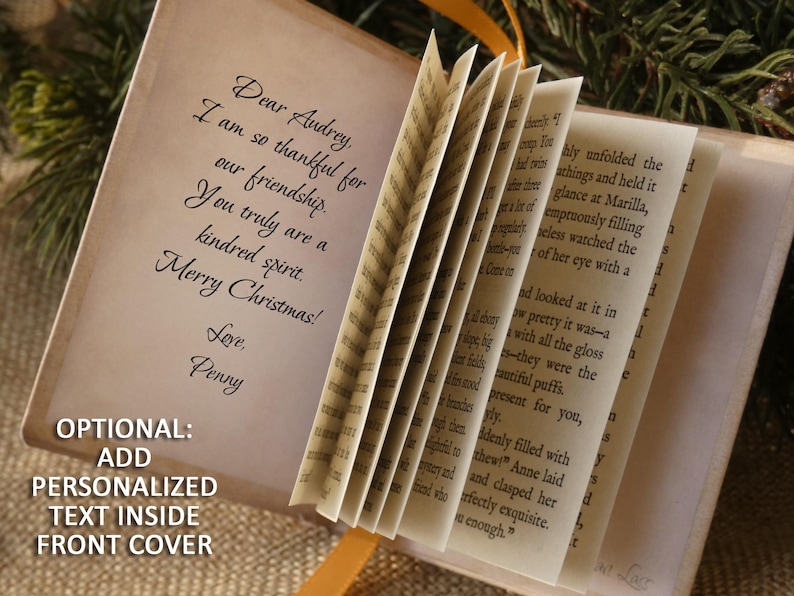May include: A miniature book with off-white pages featuring printed text. The inside front cover displays the message: Dear Audrey, I am so thankful for our friendship. You truly are a kindred spirit. Merry Christmas! Love, Penny. The book has a yellow ribbon.