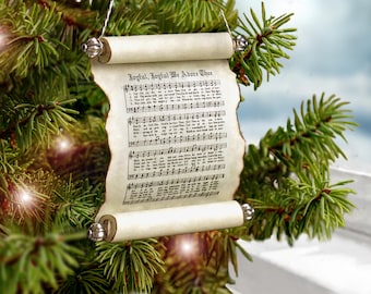 May include: A scroll-shaped Christmas ornament featuring the printed lyrics and musical notation for the hymn Joyful, Joyful We Adore Thee. The paper has a cream-colored, aged appearance with dark, burnt-looking edges and silver end caps.