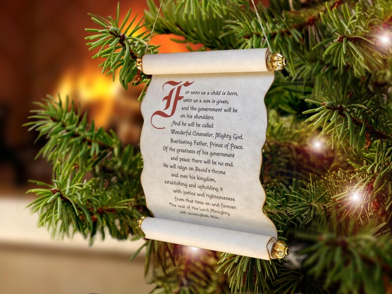 May include: A hanging scroll ornament featuring a parchment-style paper with a decorative red initial letter and black printed text that reads For unto us a child is born, unto us a son is given, and the government will be on his shoulders.