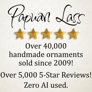 May include: The text Papuan Lass is written in black script above five gold stars. Below this, the text reads: Over 40,000 handmade ornaments sold since 2009! Over 5,000 5-Star Reviews! Zero AI used. The background is a light, textured off-white.