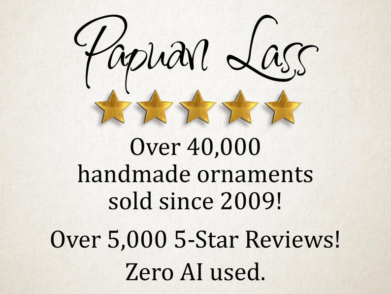 May include: The text Papuan Lass is written in black script above five gold stars. Below this, the text reads: Over 40,000 handmade ornaments sold since 2009! Over 5,000 5-Star Reviews! Zero AI used. The background is a light, textured off-white.