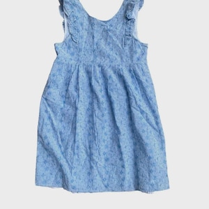 May include: A sleeveless dress in light blue and white vertical stripes featuring a delicate floral pattern throughout. The garment has a scoop neckline and ruffled shoulder straps that extend down the front bodice, creating a textured look.