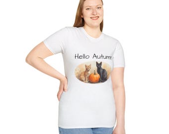 Könnte beinhalten: Weißes T-Shirt mit dem Text "Hello Autumn" und einer Grafik mit einem Kürbis, einer orangefarbenen Tabby-Katze und einer schwarzen Katze. Die Katzen sitzen neben dem Kürbis. Die Frau trägt eine blaue Jeans.