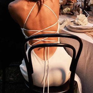 Könnte beinhalten: Ein weißes, ärmelloses Kleid mit einem Schnürrücken. Das Kleid ist in der Taille gebunden und hat einen langen, fließenden Rock.