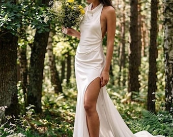 May include: A floor-length white sleeveless dress with a high neckline, a side slit, and a draped waistline. The dress features a long train and is paired with a bouquet of yellow and white flowers and simple strappy sandals.
