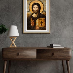 Pode incluir: Obra de arte religiosa emoldurada com um retrato de uma figura com uma aur&eacute;ola, segurando um livro. A obra de arte tem um esquema de cores dourado e castanho, com uma moldura de madeira. A imagem &eacute; exibida em uma mesa de console de madeira escura.