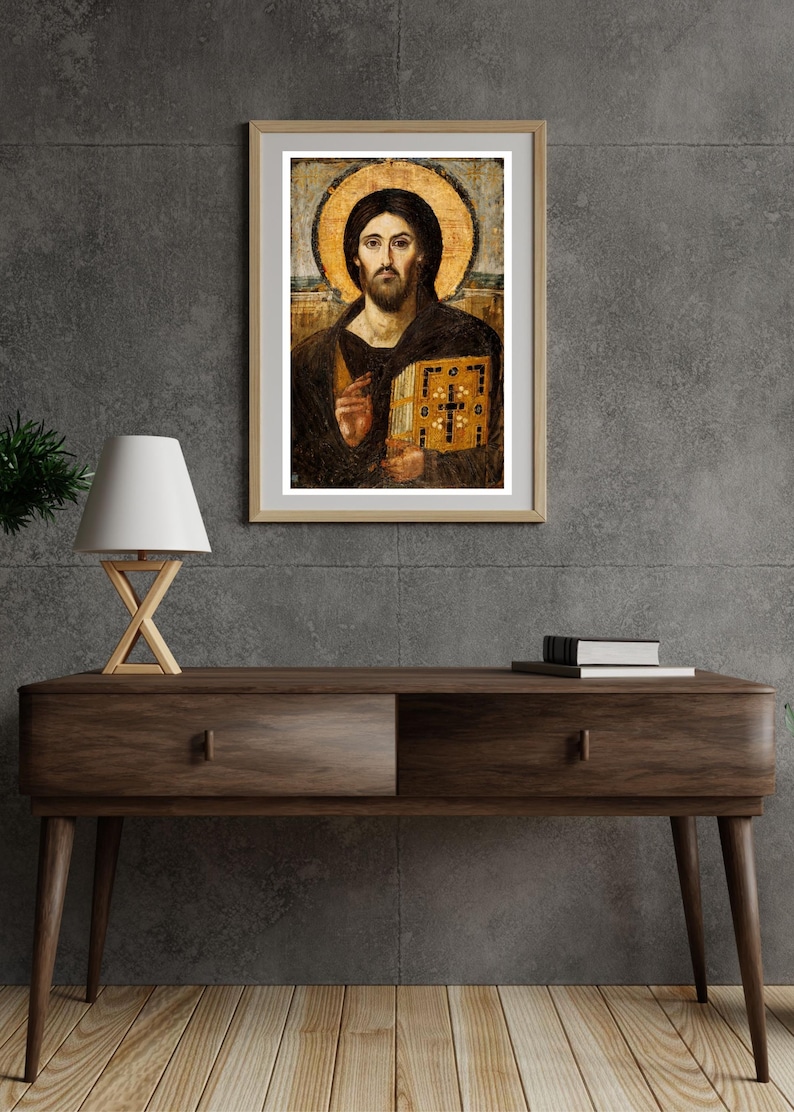 Pode incluir: Obra de arte religiosa emoldurada com um retrato de uma figura com uma aur&eacute;ola, segurando um livro. A obra de arte tem um esquema de cores dourado e castanho, com uma moldura de madeira. A imagem &eacute; exibida em uma mesa de console de madeira escura.