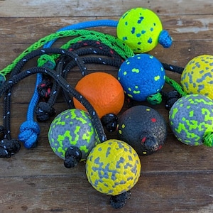 May include: Nine colourful balls with rope handles. The balls are speckled with different colours, including green, blue, yellow, orange, and black. The ropes are black, blue, and green.