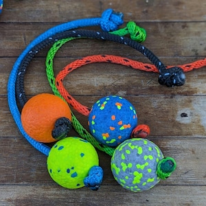 May include: Four colorful balls with ropes attached. The balls are covered in a textured material and have different colored spots. The ropes are blue, black, green, and orange.