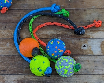Könnte beinhalten: Eine Auswahl an Hundespielzeugen mit strukturierten Bällen und geflochtenen Seilgriffen. Die Bälle sind in verschiedenen Farben erhältlich, darunter Orange, Blau, Grün und Grau, mit kontrastierenden Sprenkeln. Die Seile sind blau, schwarz, grün und rot.